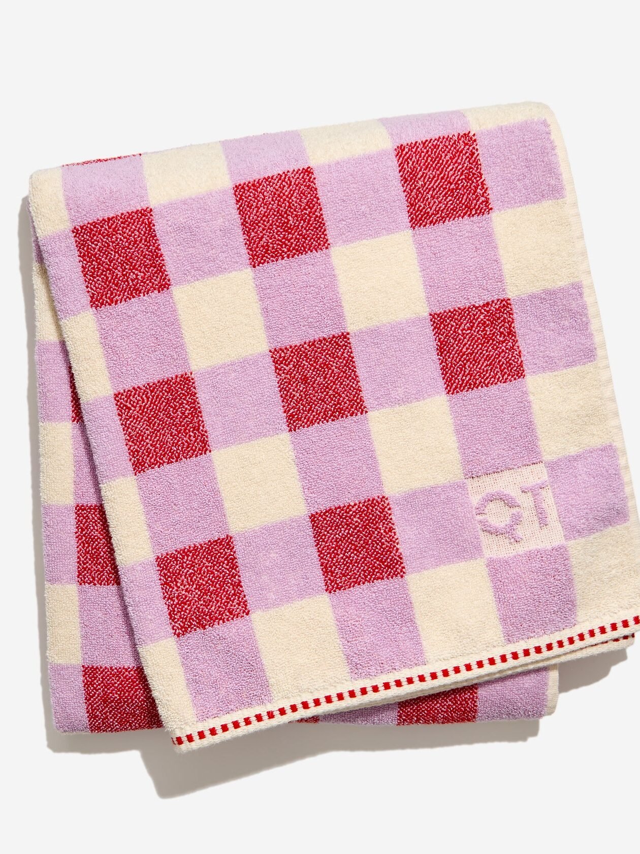 A folded organic towel with a red, lavender, and cream checkerboard pattern and a small embroidered "QT" on the cream square.