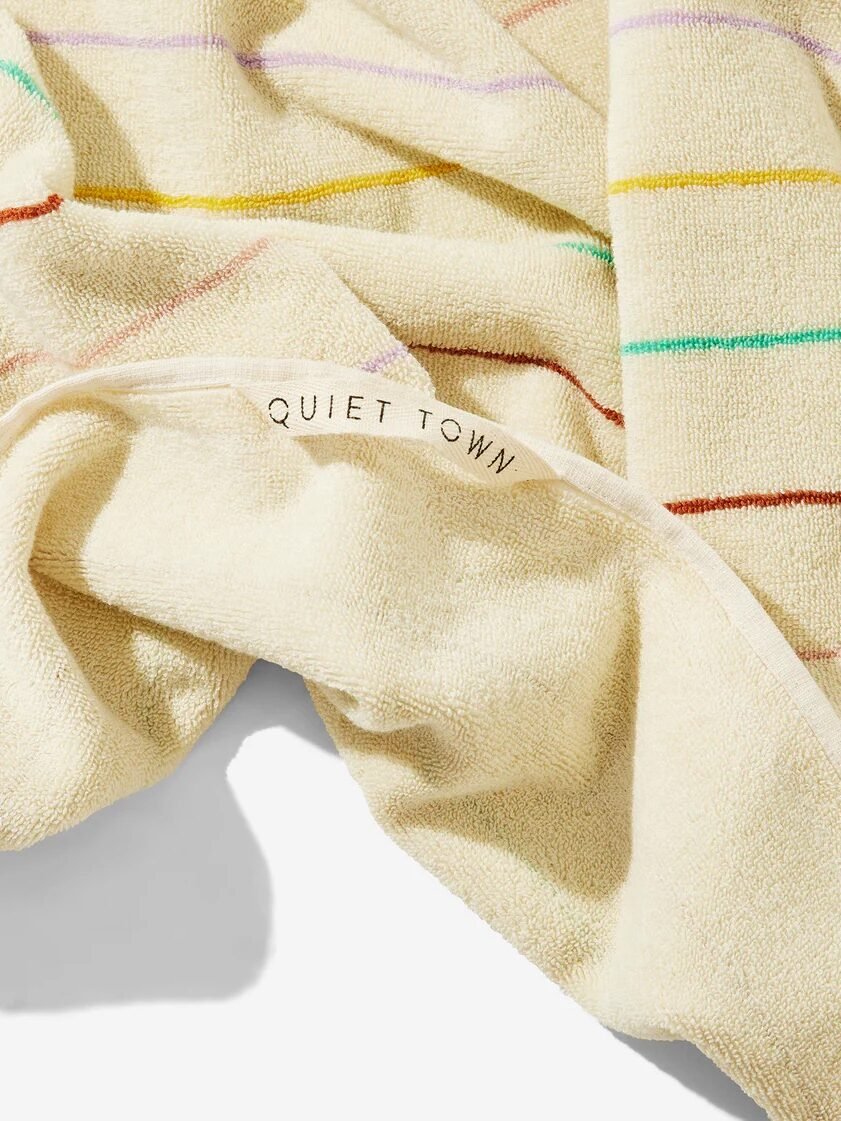 A cream-colored organic towel with multicolored stripes and a sewn-in label reading "QUIET TOWN" rests on a white surface.