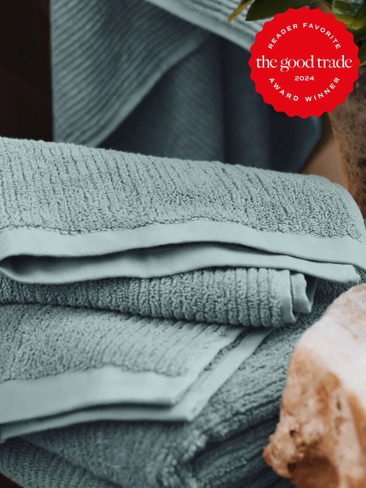 Folded light blue organic towels stacked neatly on a surface with a red award badge in the top right corner that reads "The Good Trade Reader Favorite Award Winner 2024.