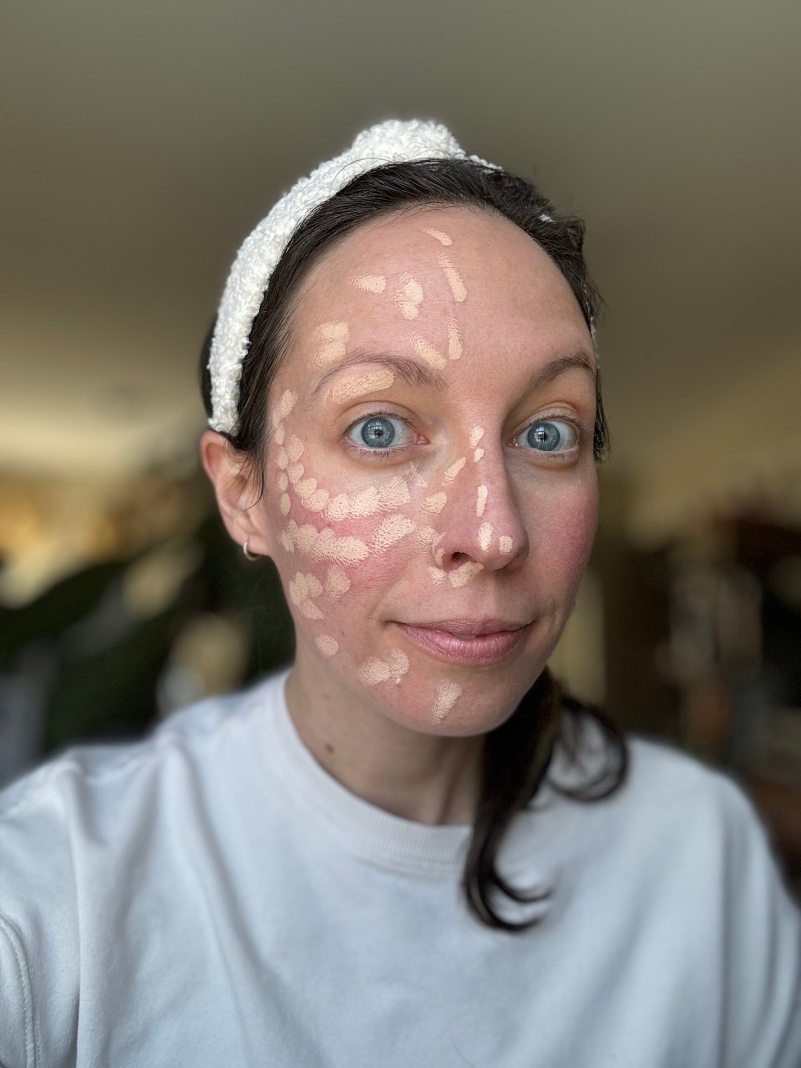 A person with a headband applying foundation makeup on their face.