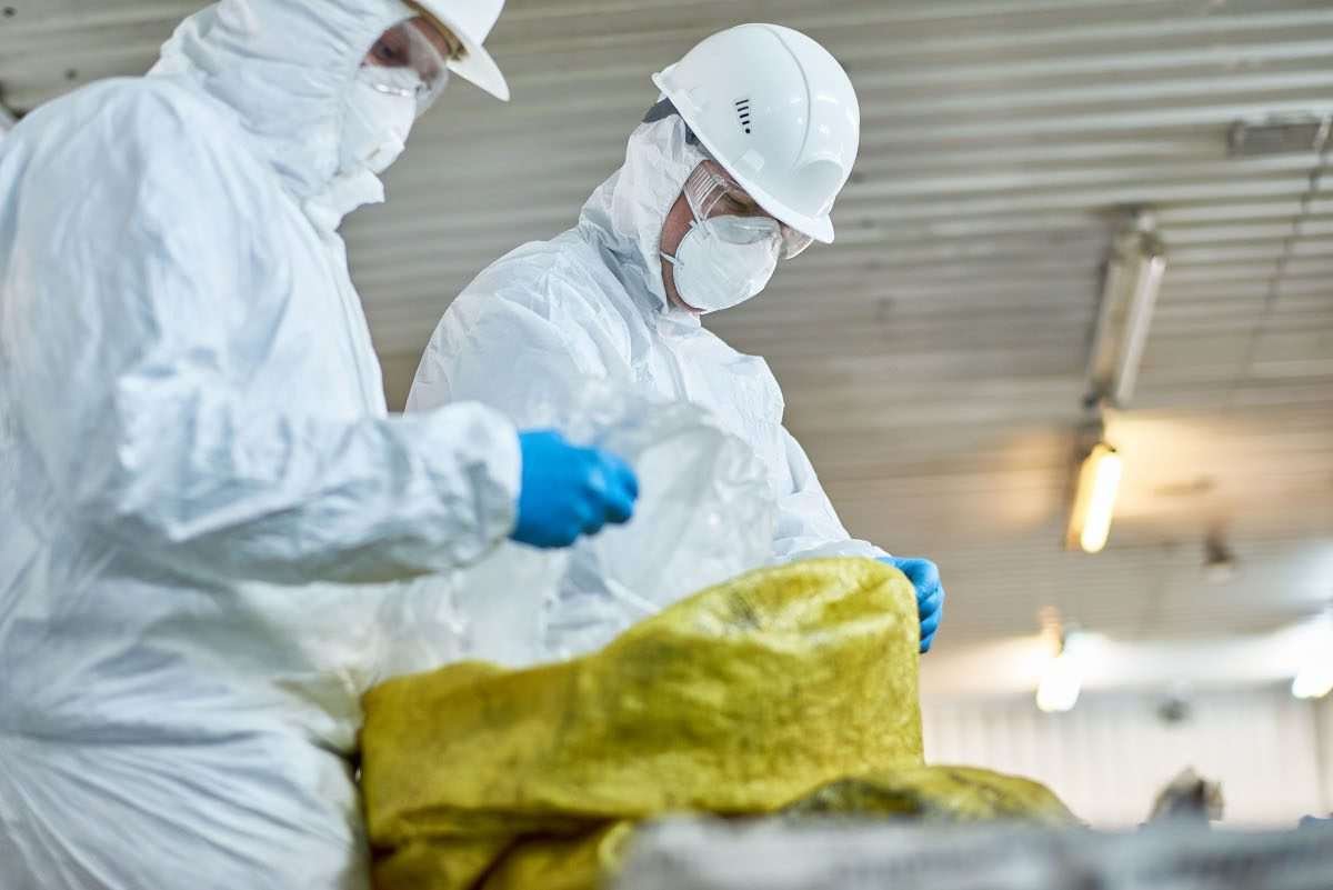 Standing figures in hazmat suits looking downwards to inspect materials or indistinct objects