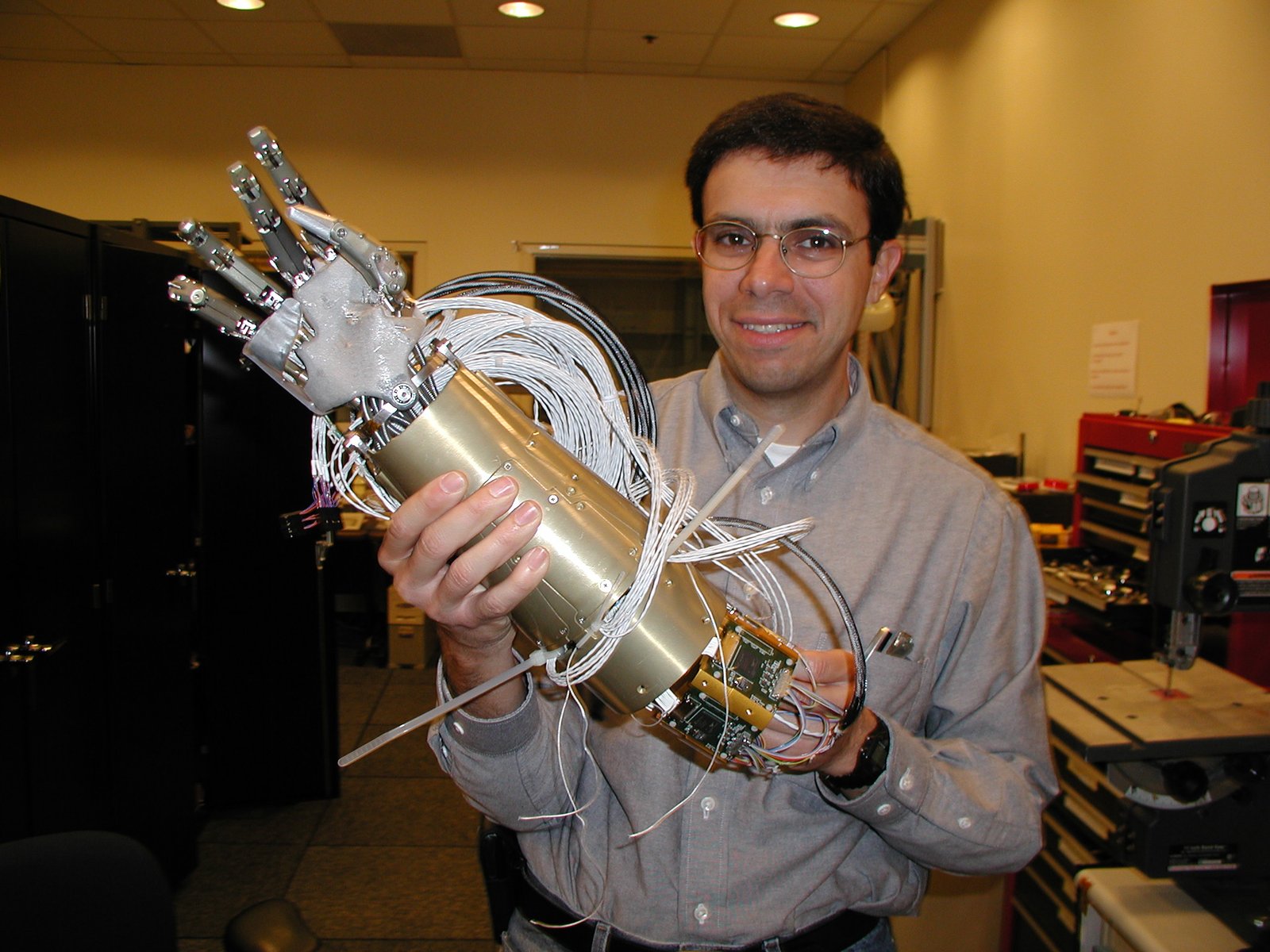 In a yellow-lit room, Myron Diftler holds a robotic arm