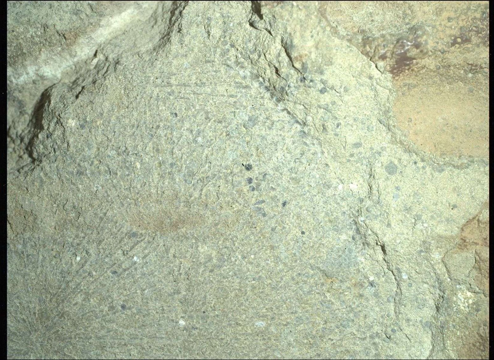 A color close-up photo of the Martian surface shows a pale yellowish-tan rock, with grooves or lines emanating from a center point like rays, with scattered black spots and small indentations throughout its surface.