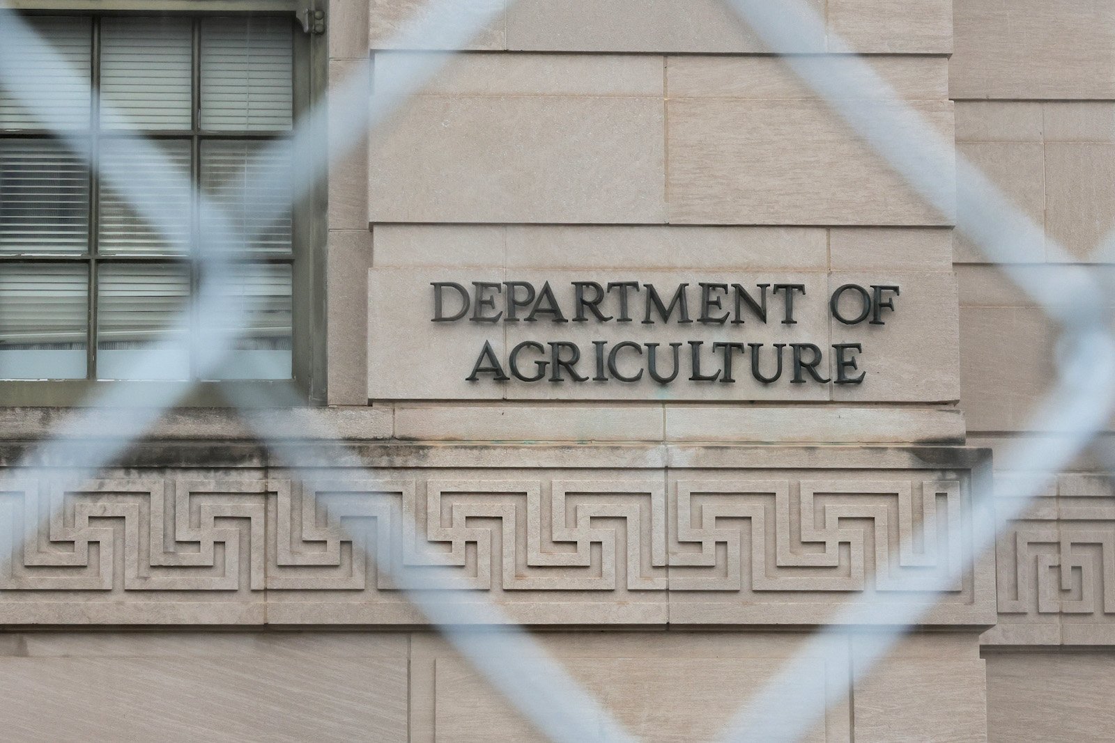 a sign on a building says department of agriculture, as seen through a chain-link fence