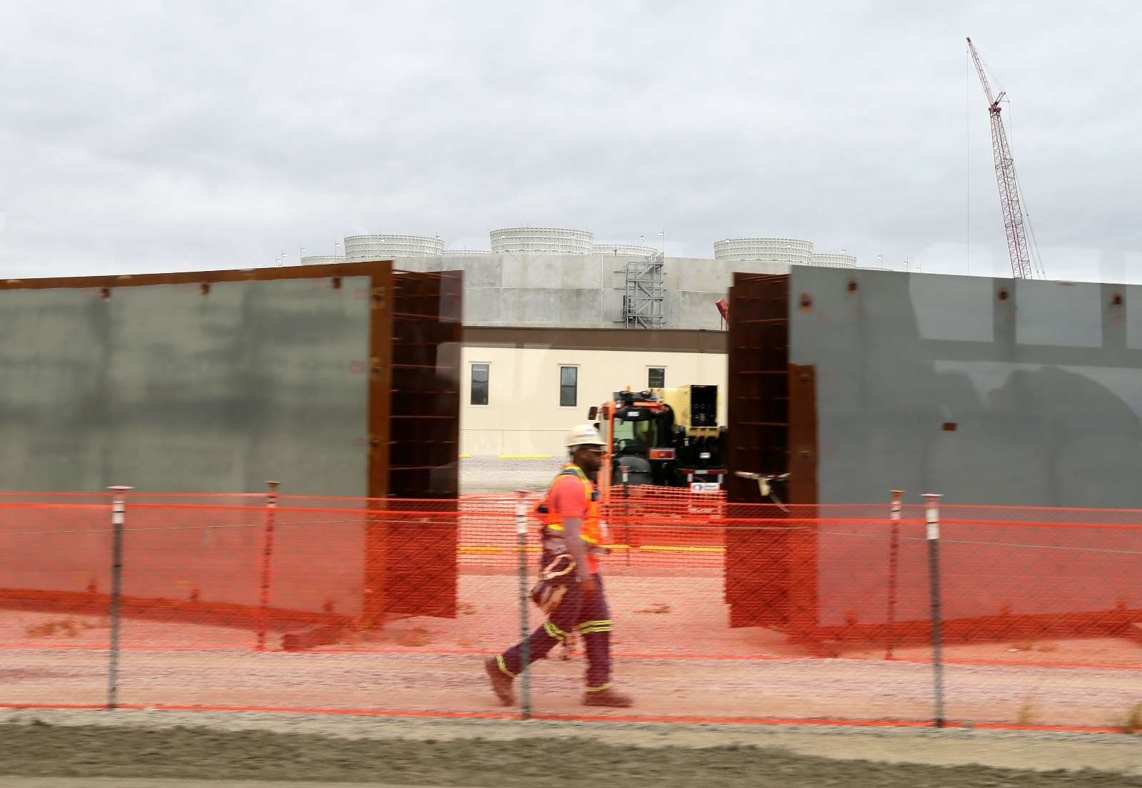 A worker wearing a hard hat and safety vest walks past the cooling towers of a power plant under construction.