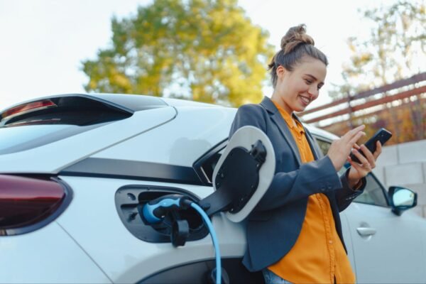 A woman standing next to her EV car while it charges
