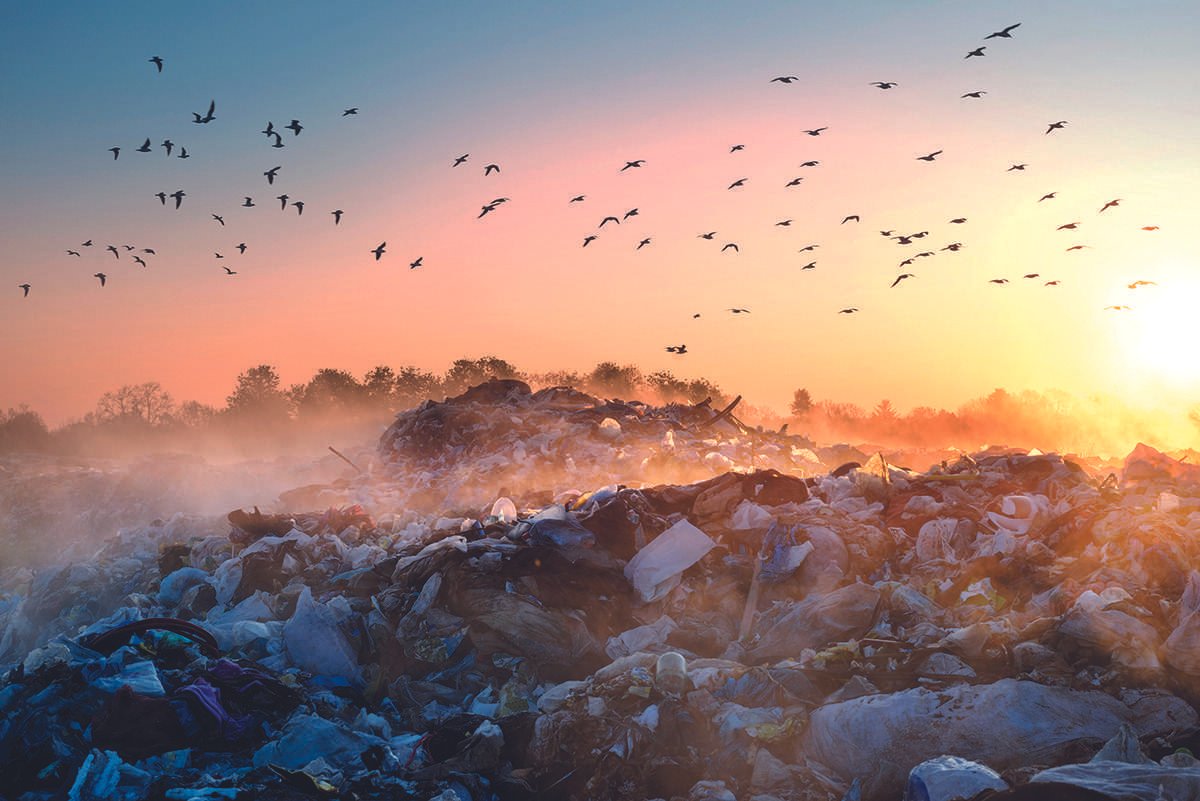 A landfill site with dust hovering above the ground and violet-orange sunlight in background