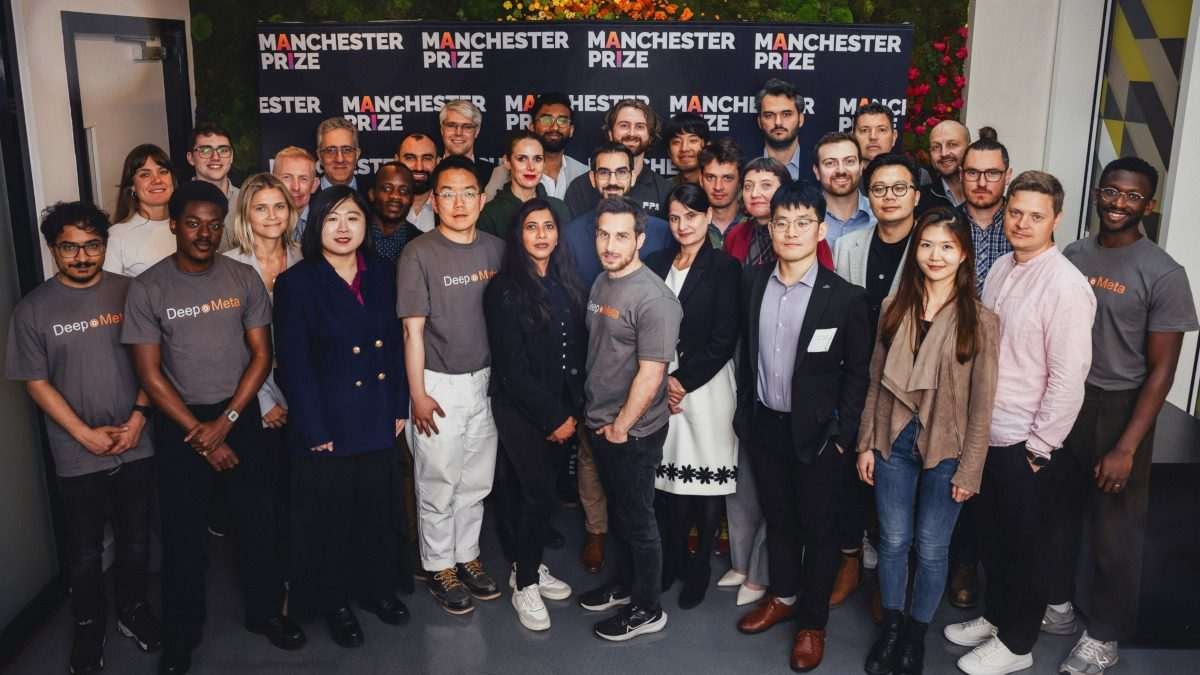 A full stage of 30 or so people, a mix of ethnicities and genders, in smart casual clothing, looking towards the camera, and in the background the words MANCHESTER PRIZE are visible