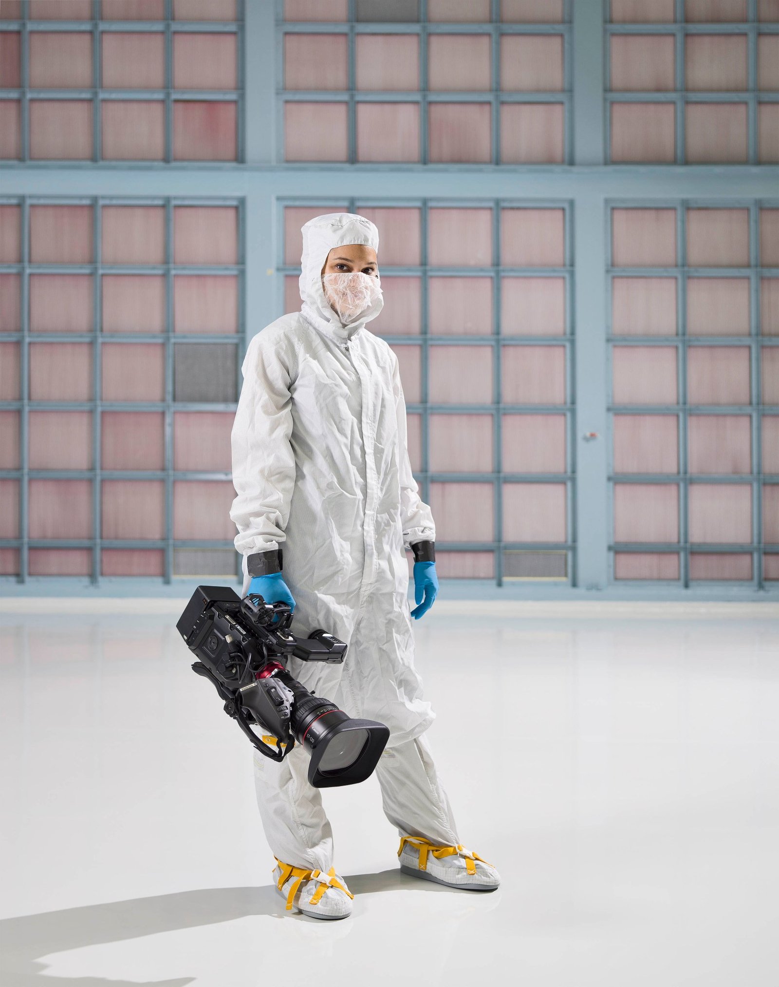 A photo of Sophia Roberts in a white bunny suit in the Goddard clean room holding a video camera