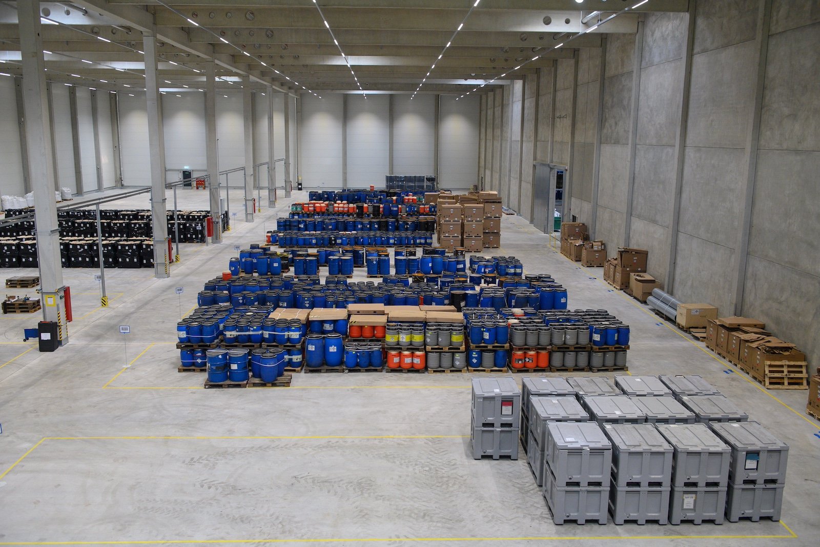 An aerial view of a large industrial space containing neatly arranged barrels, boxes, and storage bins
