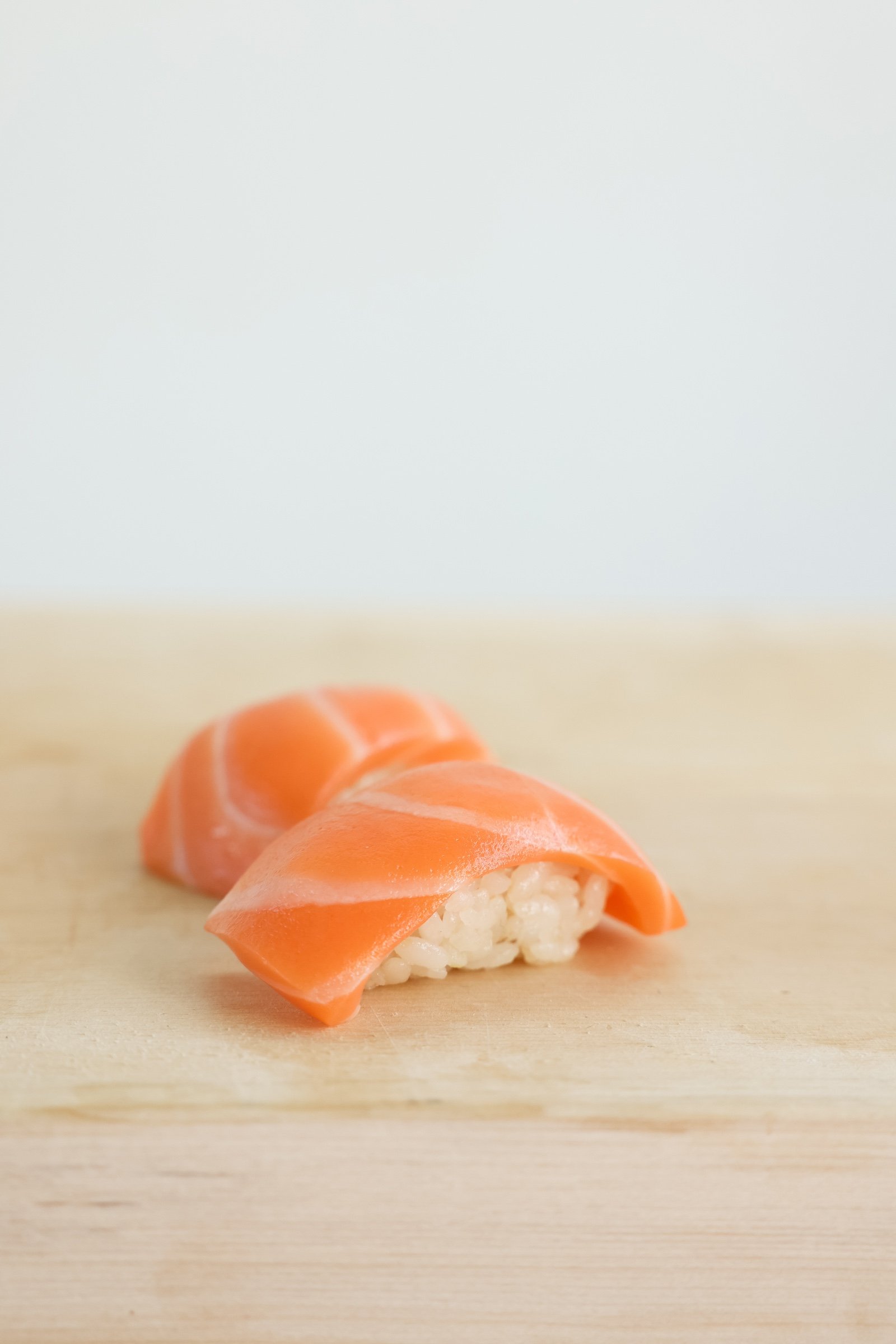 Two slices of raw, orange salmon rest atop mounds of sushi rice on a wooden surface