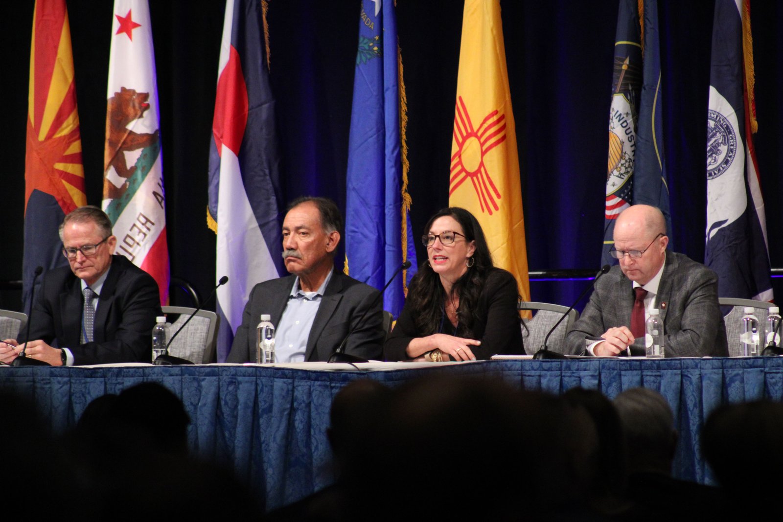 Three men and a woman sit at a table in front of a series of flags
