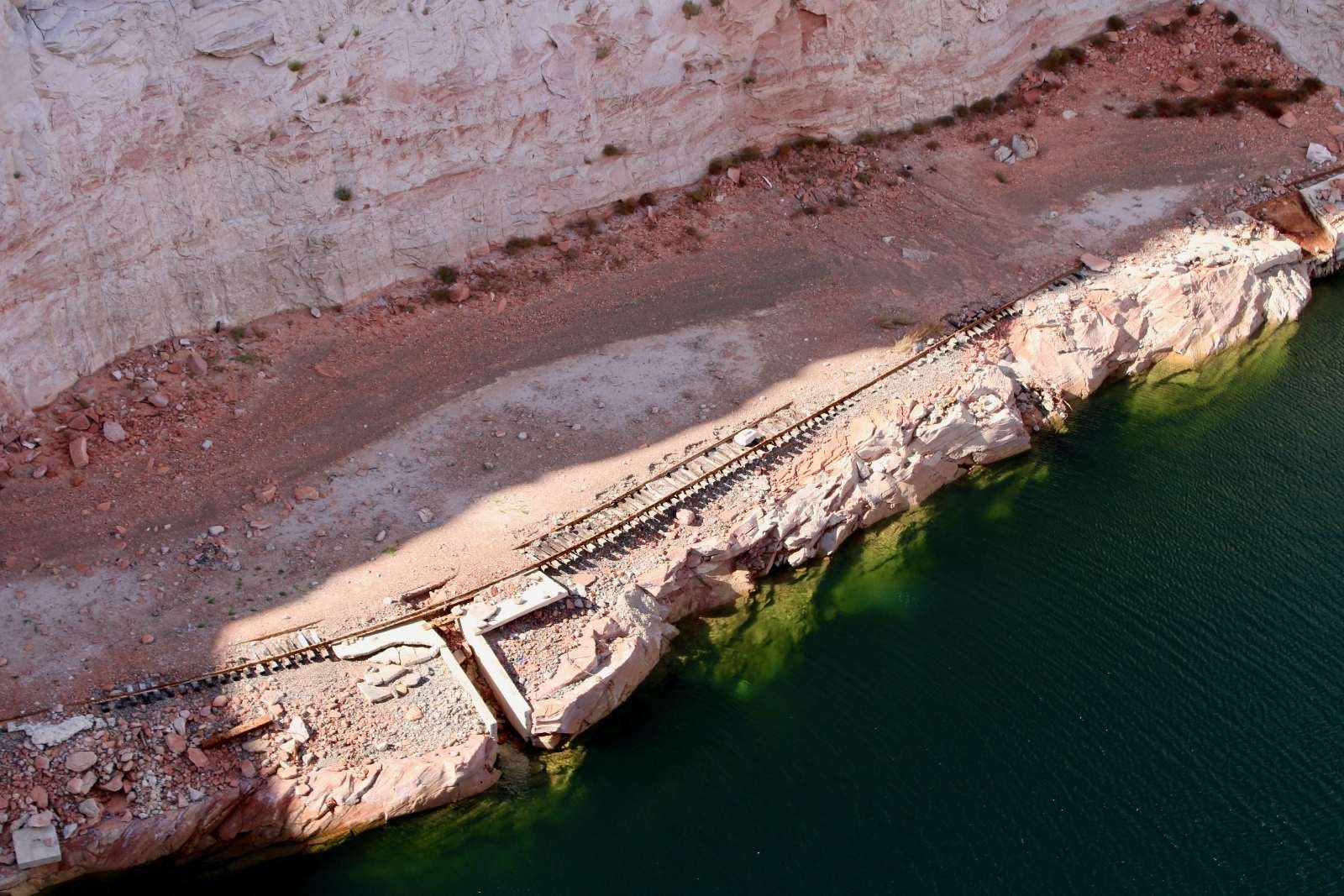 An aerial view of train tracks running through red rocks next to water