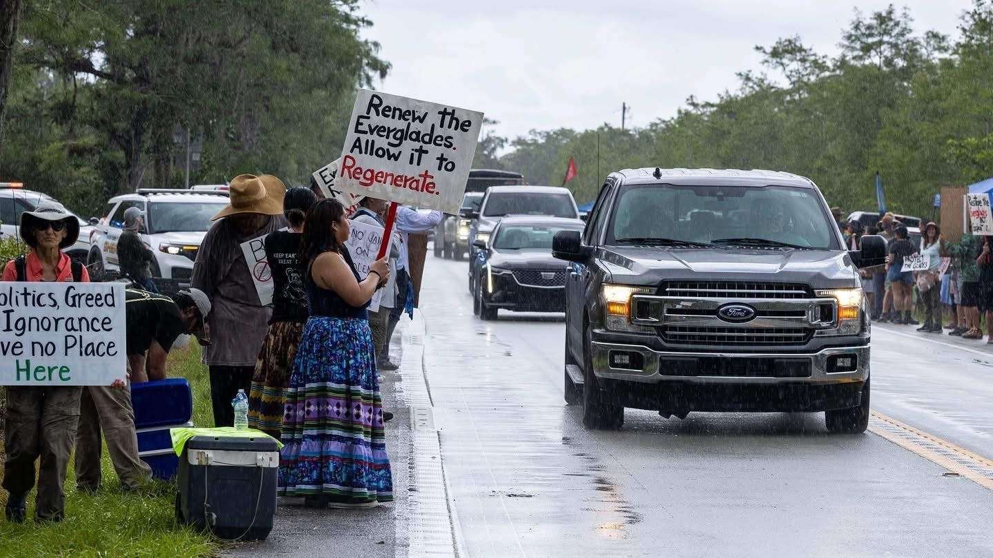 Protestors stand outside detention center as vehicles drive by