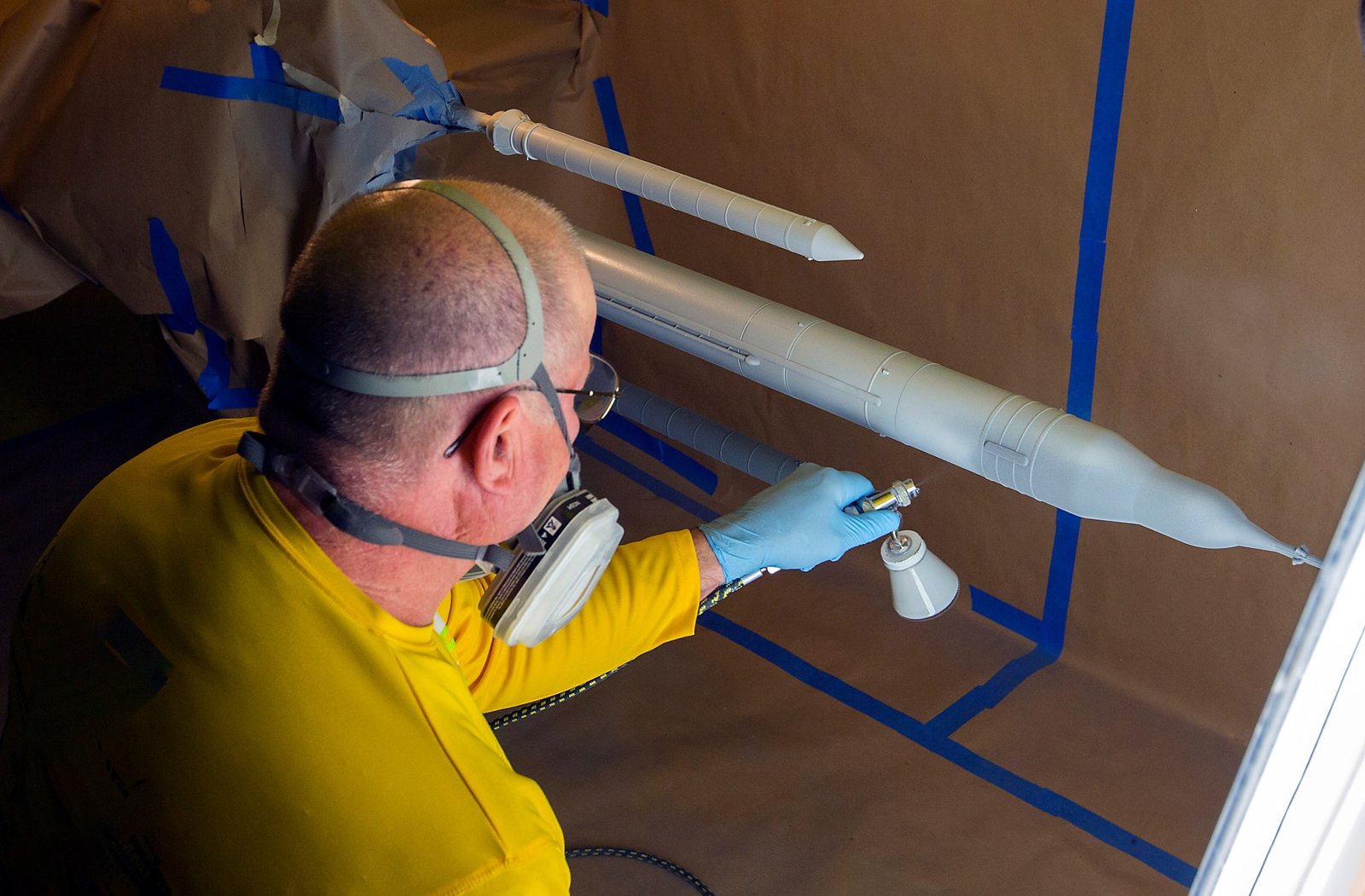 A technician sprays pressure sensitive paint onto a small model of the Space Launch System rocket.