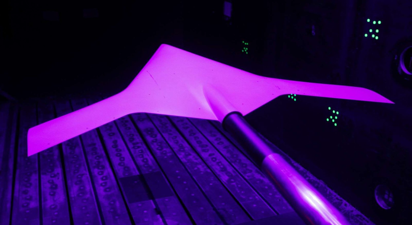 A model of a blended wing aircraft glows pink inside a wind tunnel.