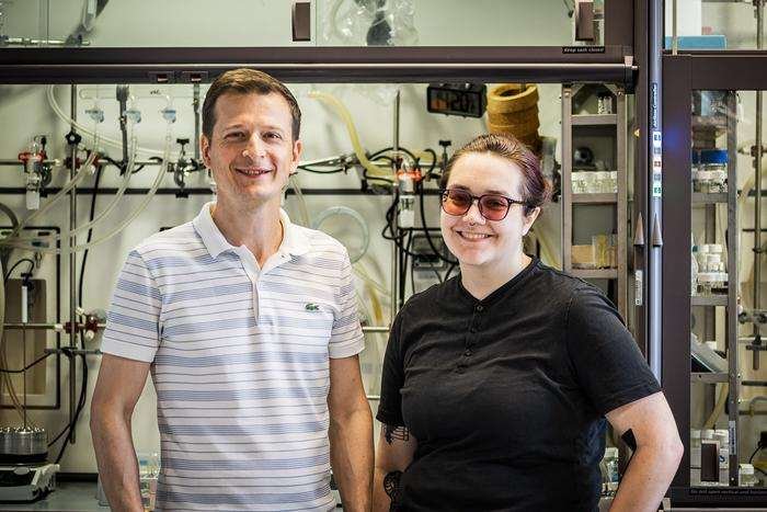 A young man and young woman in casual clothes smile at the camera in a setting that looks like a scientific laboratory