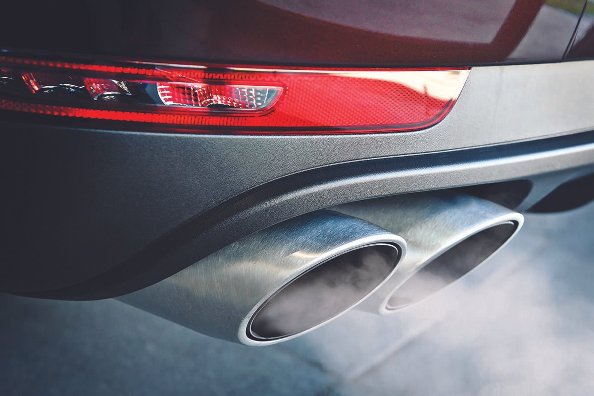 Modern-looking car exhaust, a cylindrical pipe structure seen within surrounding parts of the vehicle including a portion of the back bumper and left-side tail light