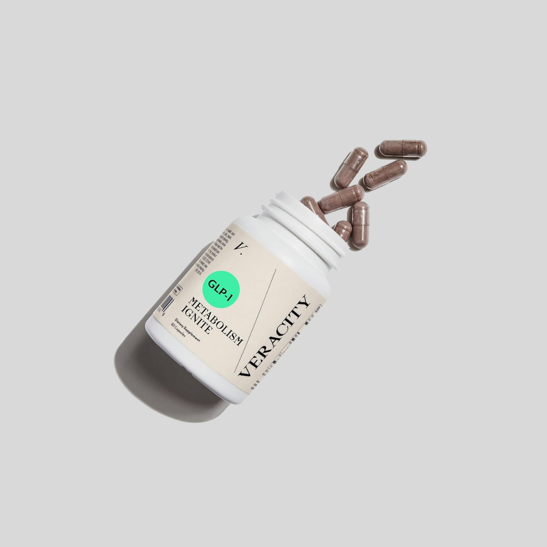 A white bottle labeled "Veracity Metabolism Ignite" lies on its side with several brown capsules spilling out onto a light gray background.
