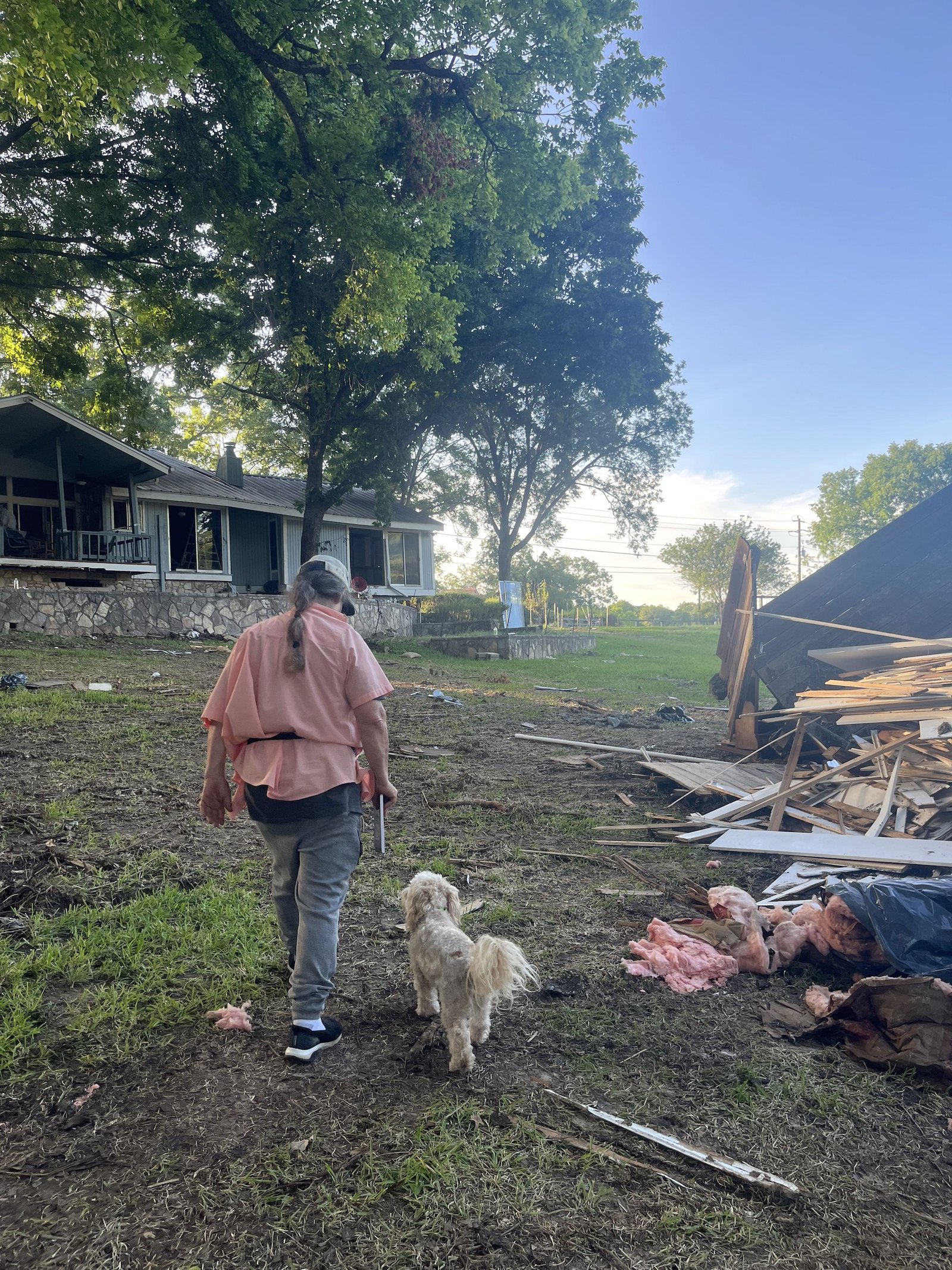 a man and his dog walk near a pile of debris and a house after a flood