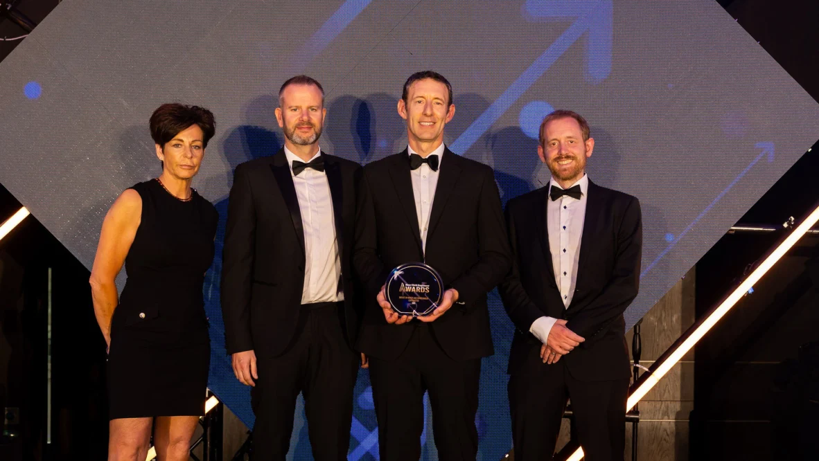 Four people in evening dress, one of them holding an award, look towards the camera