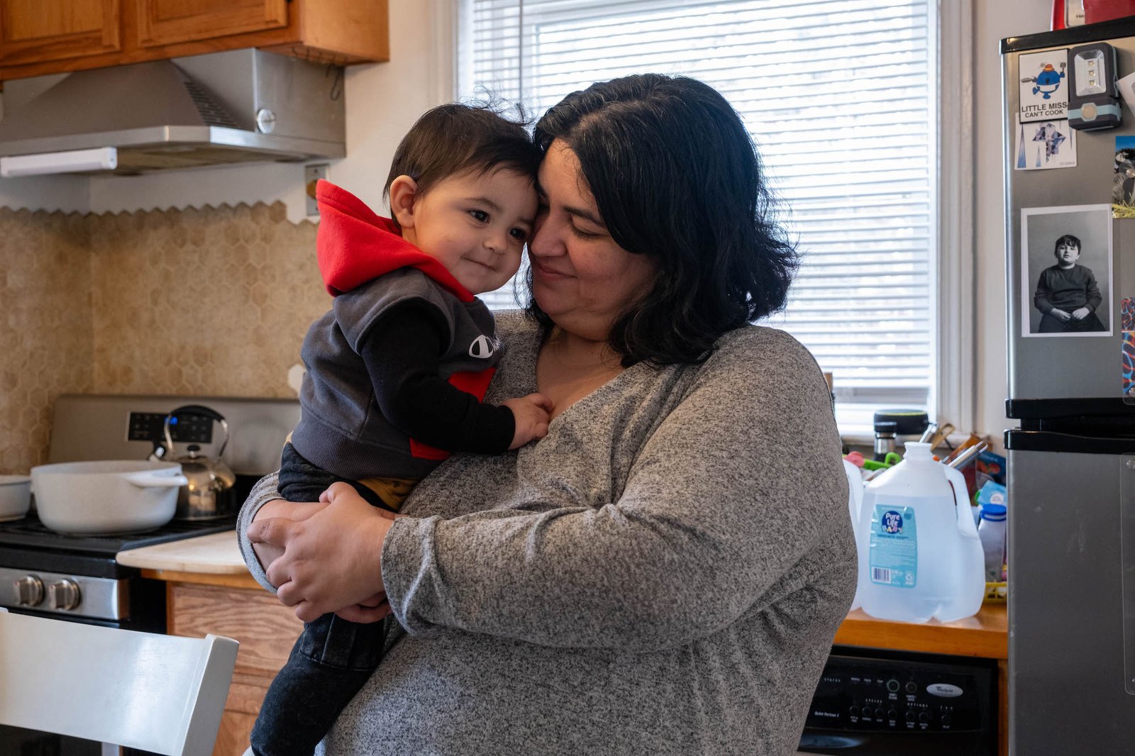 A woman cuddles with a toddler in her kitchen