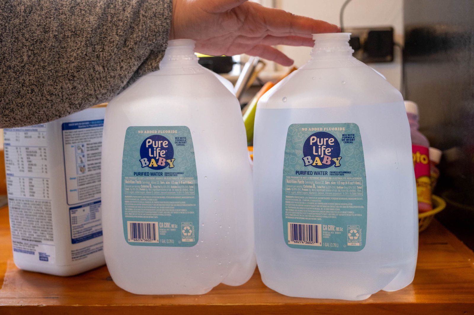 a hand touches the top of one of two plastic jugs of water on a kitchen counter