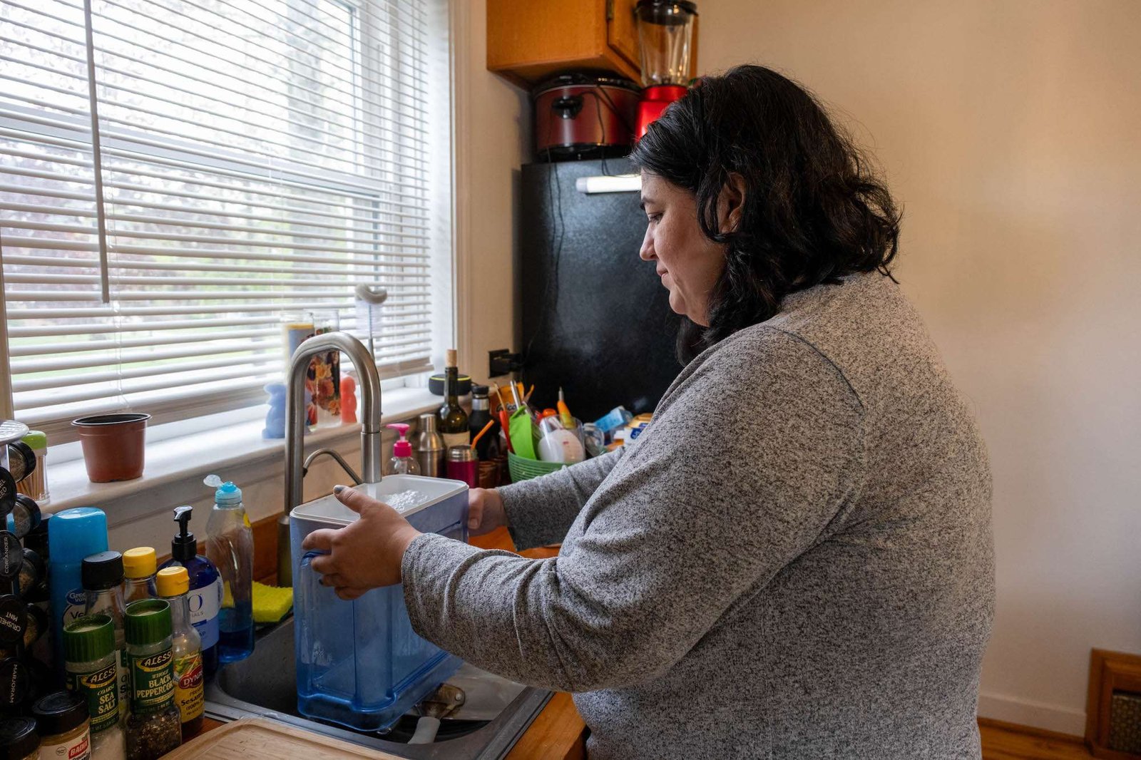 A woman fills a water filter with tap water in a kitchen