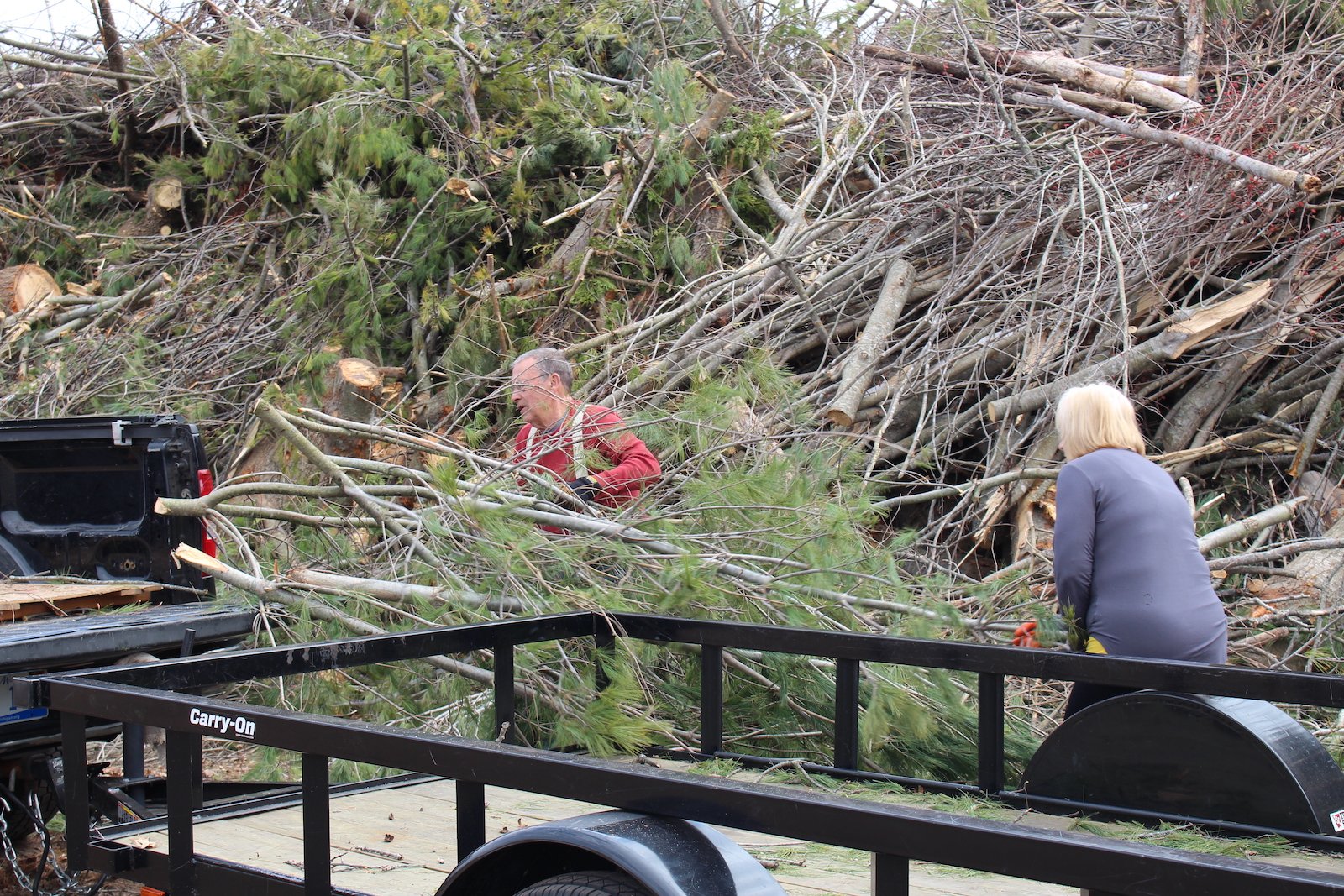 a man and woman feed giant piles of wood into a drop off area