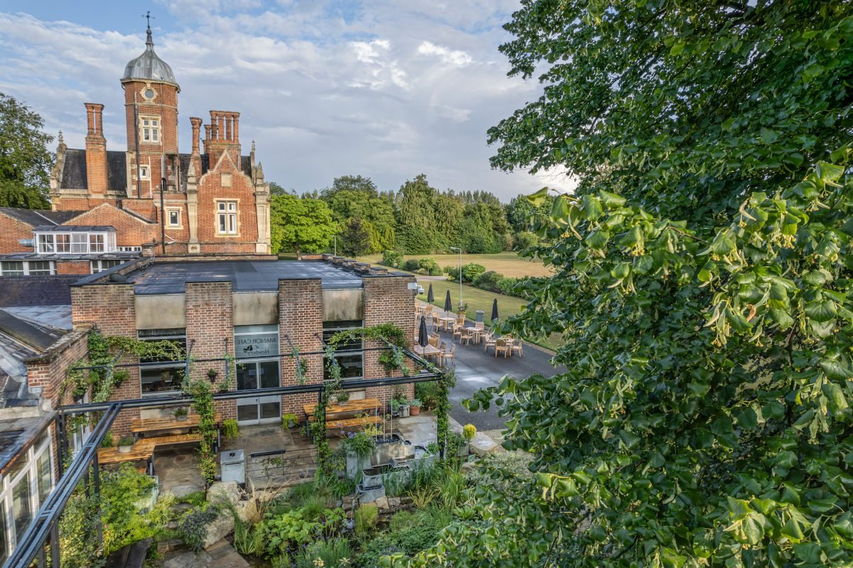 Treetop view across the top of a garden situated outside an Elizabethan-style mansion with a tall central tower within the structure