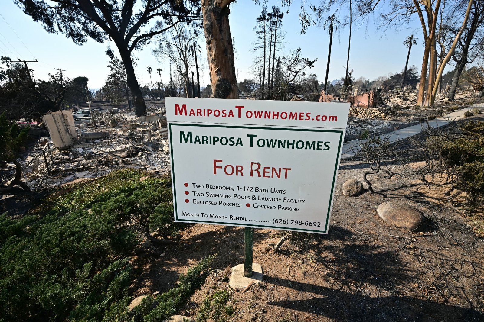 The remains of townhomes destroyed by the Eaton Fire lie behind an advertising sign in Altadena, California, on January 10, 2025. Massive wildfires that engulfed whole neighborhoods and displaced thousands in Los Angeles have killed at least 10 people, authorities said, as California's National Guard soldiers readied to hit the streets to help quell disorder. News of the growing toll, announced late Thursday January 9 by the Los Angeles County Medical Examiner, came as swaths of the United States' second-largest city lay in ruins.