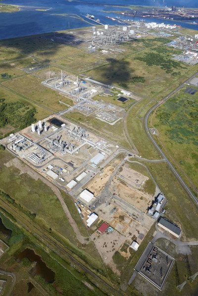An industrial site as viewed from high in the air, with multiple differently-sized buildings visible below, all situated within a close-to-rectangular-shaped area of land in a flat location