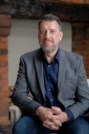 A man, seated, in business attire smiles at the camera