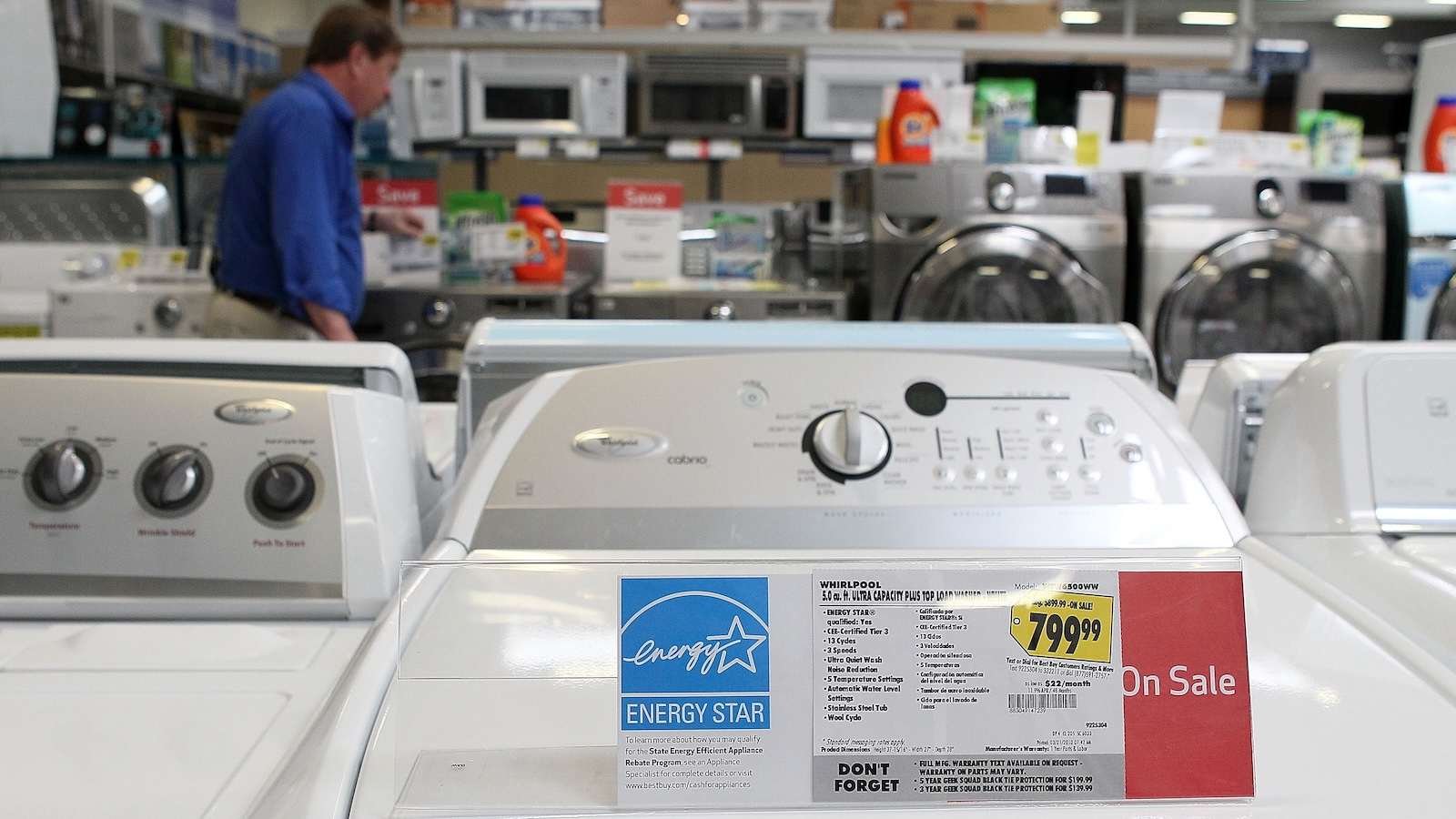 An Energy Star label is displayed on a new washing machine at a Best Buy store as a shopper in the background considers washing machines.