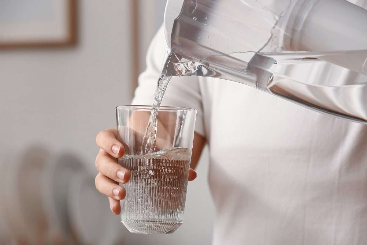 Woman's hand holding glass of water into which is being poured water from a transparent jug, which the woman also seems to be holding