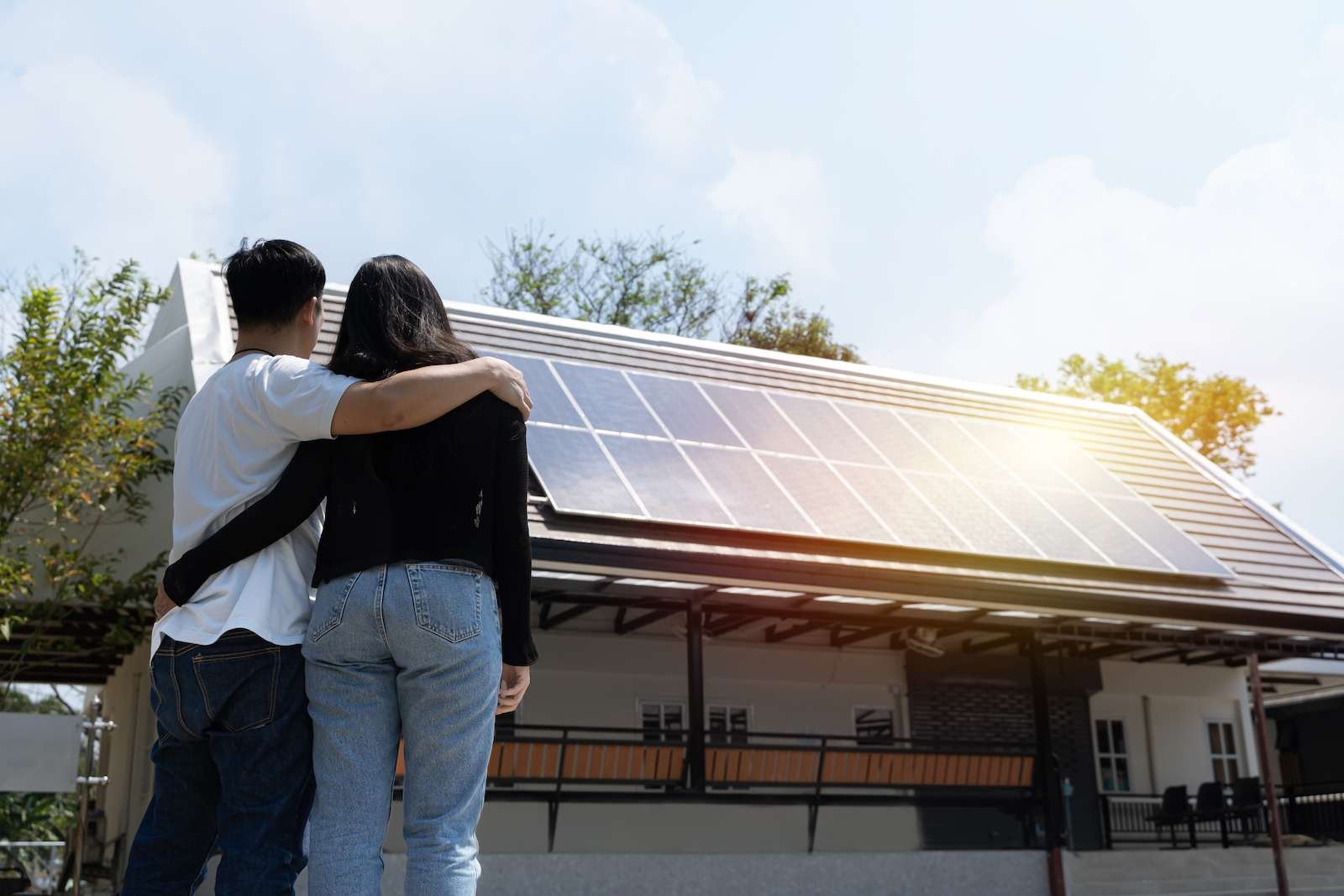 Family uses renewable energy system with solar panel. Happy couple standying near their house with solar panels. Alternative energy, saving resources and sustainable lifestyle concept.