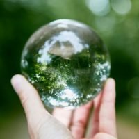 A hand holding a glass sphere against a background of greenery