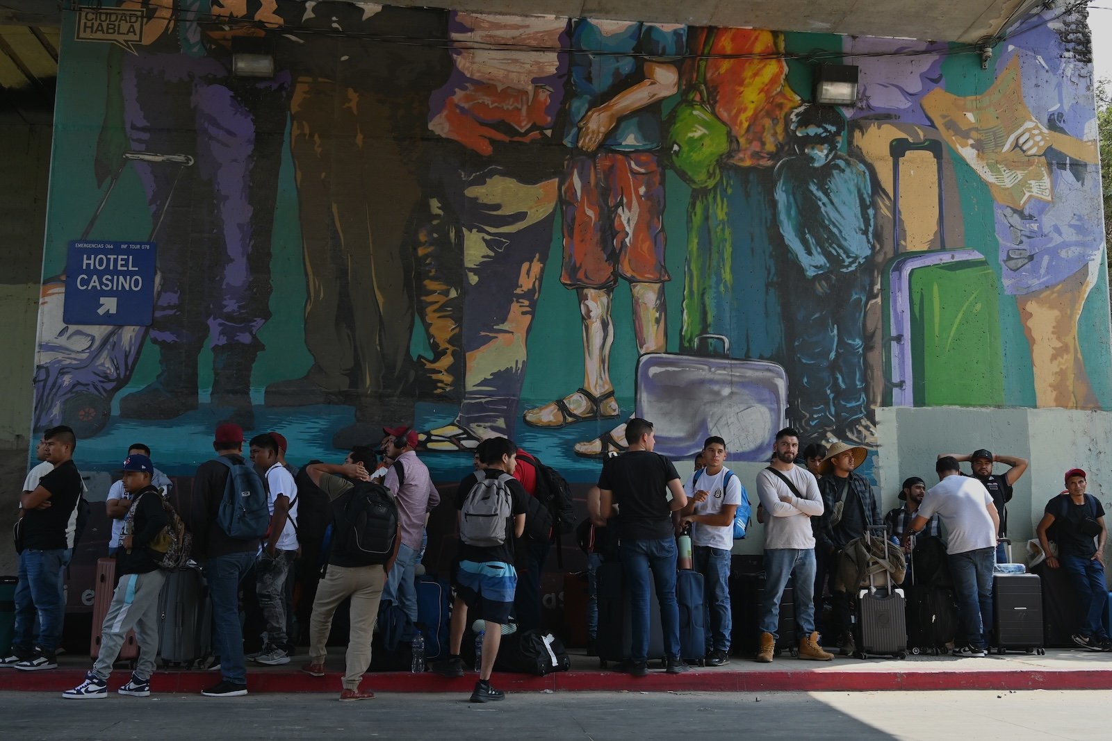 Mexican guest workers, mostly men with backpacks and suitcases, line up along a mural in Tijuana as they await entry into the U.S.