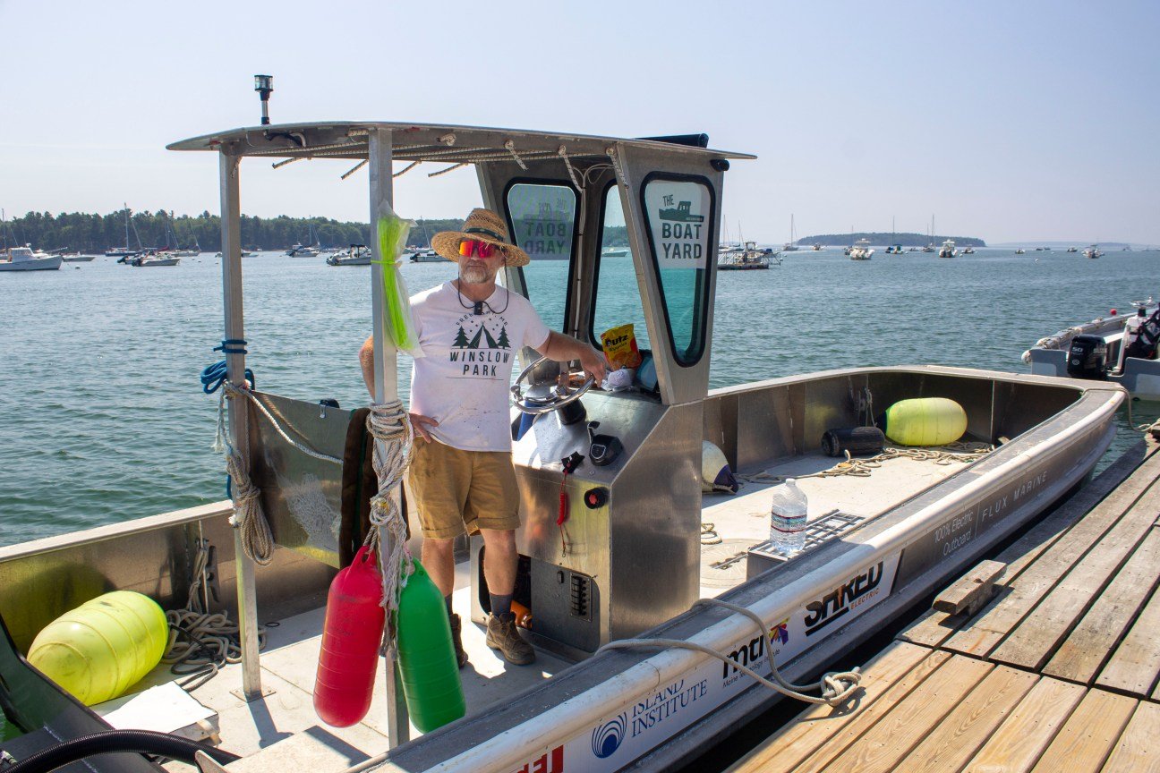 A man in a white shirt and panama hat stands aboard a small boat