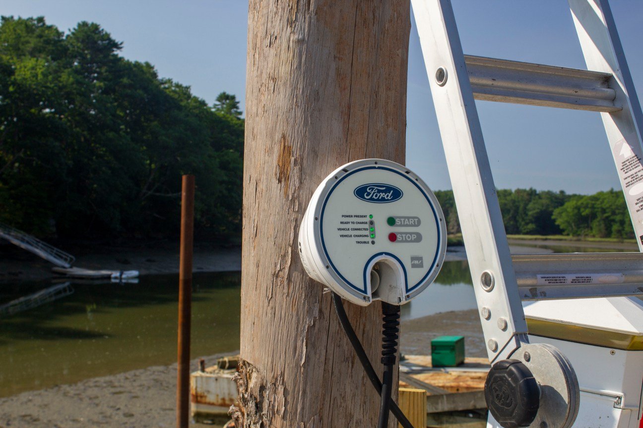 A circular charger is affixed to an electrical post in front of the water