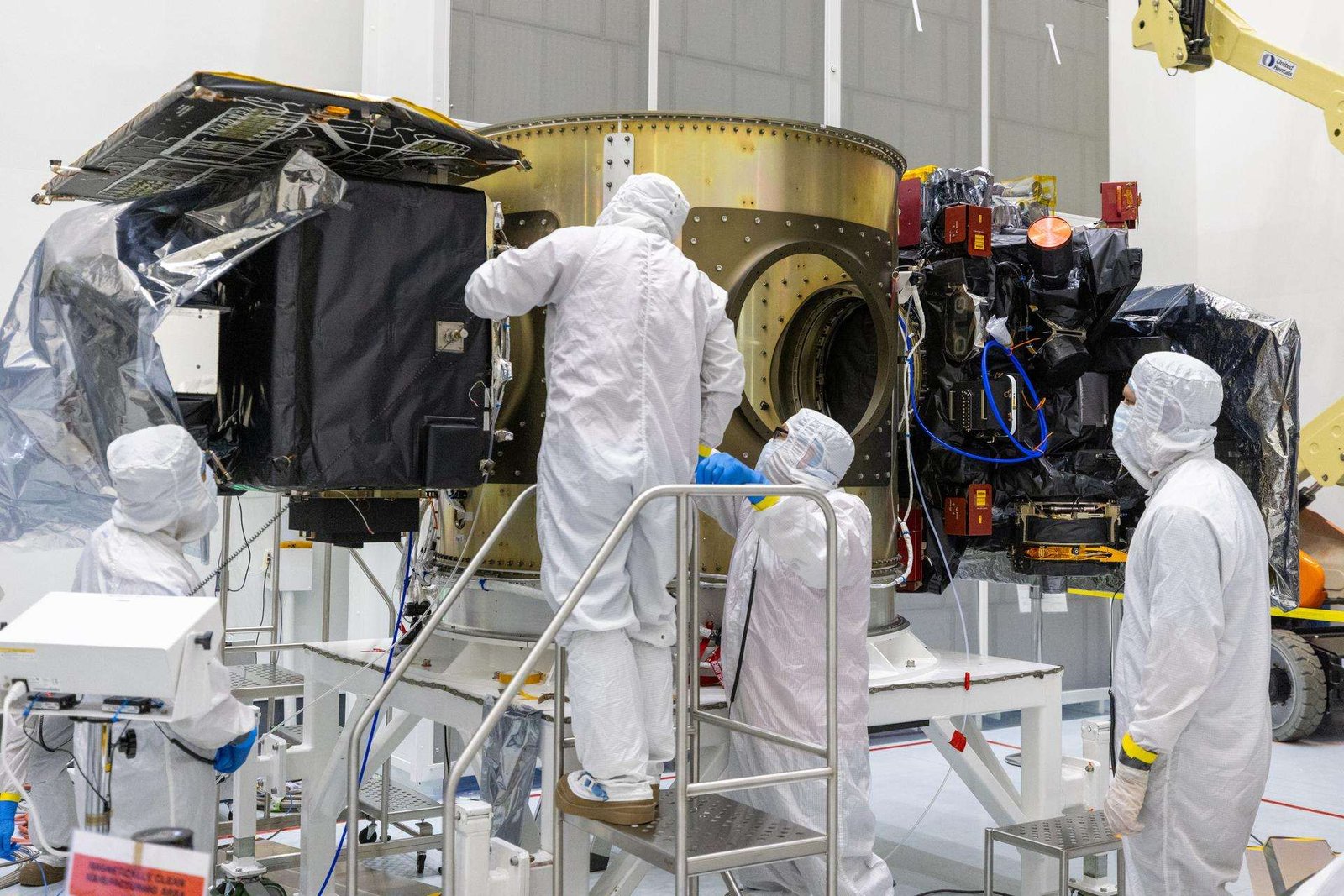 Image shows four people wearing white protective suits, commonly known as bunny suits, standing around NASA’s Carruthers Geocorona Observatory and the National Oceanic and Atmospheric Administration’s (NOAA) Space Weather Follow-On Lagrange 1 (SWFO-L1) satellite spacecraft's set to launch with NASA's IMAP (Interstellar Mapping and Acceleration Probe) observatory at NASA's Kennedy Space Center in Florida.