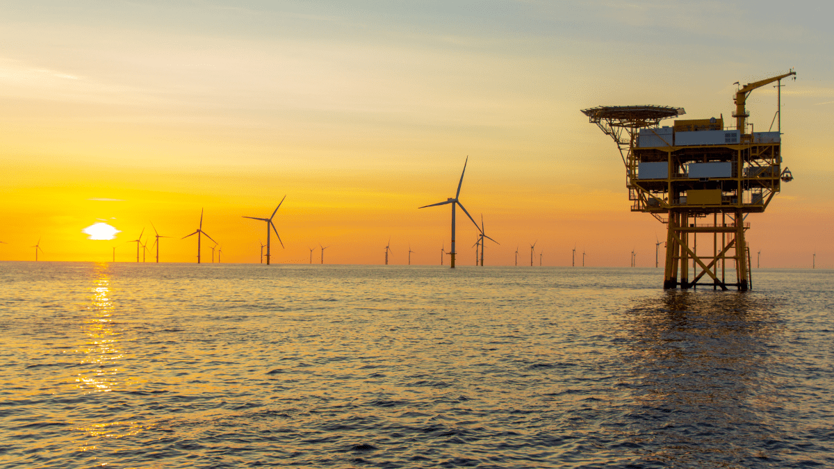 Offshore wind turbines visible at various distances on the open water, as the image approaches the horizon, with a large oil-rig-like maintenance platform visible in the foreground