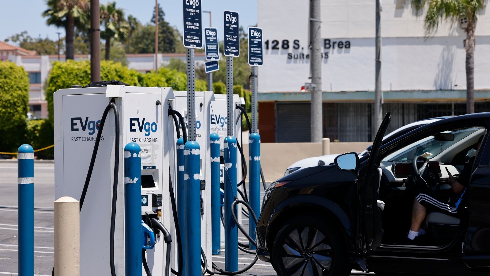A series of white and blue chargers stand next to a car in a parking lot