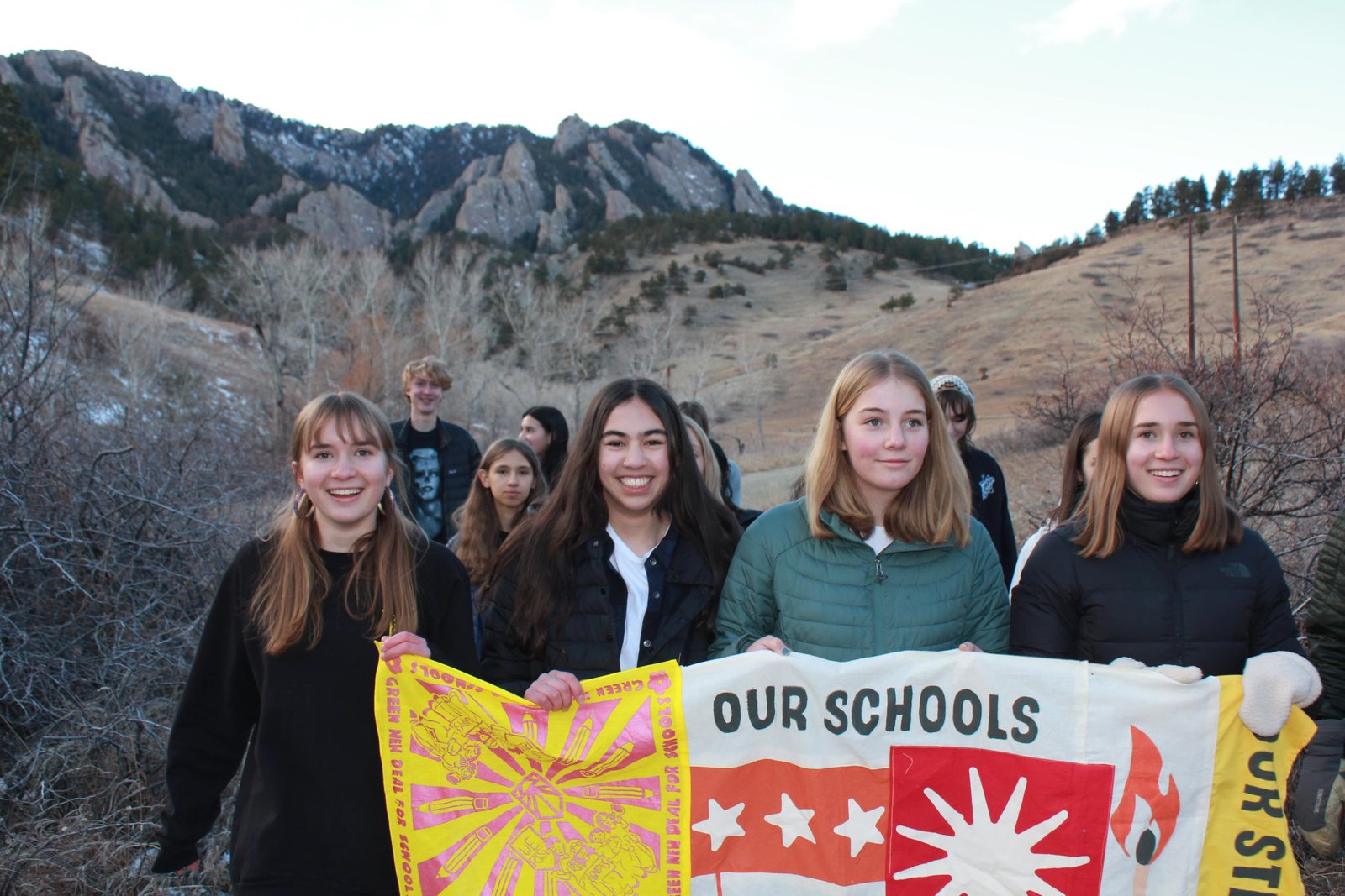 A group of teenage girls with a sign stand smiling in front of mountains