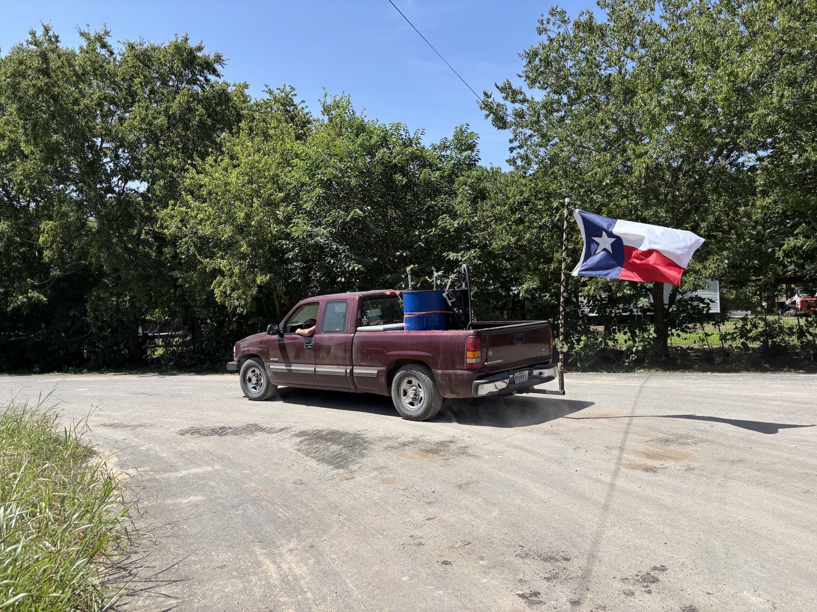 a truck with a Texas flag on the back drives on a rural road