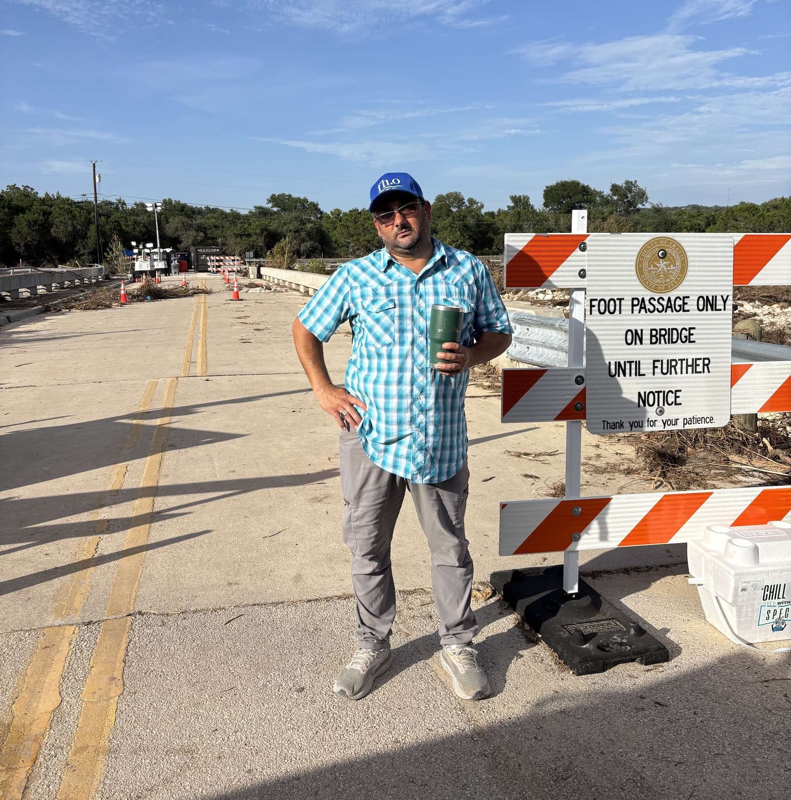 a man in a blue baseball cap stands in front of a no crossing barrier on a bridge