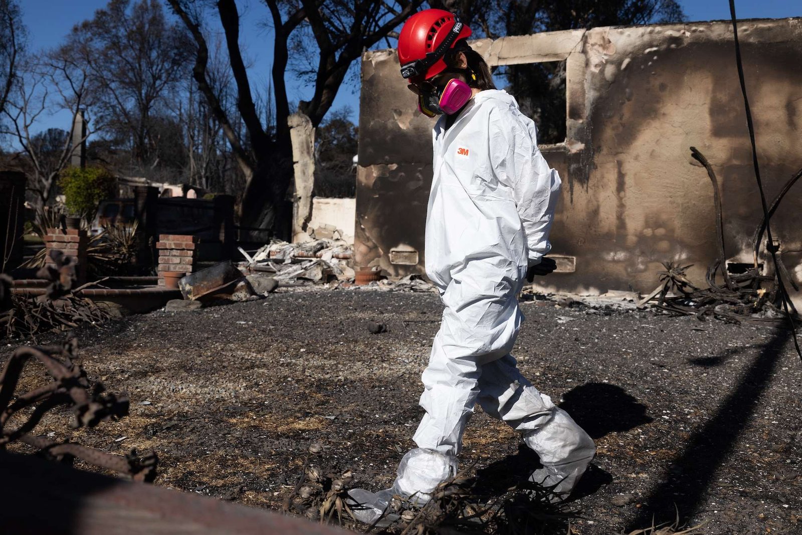 A woman in a hazmat suits walks through the burned remnants of a house