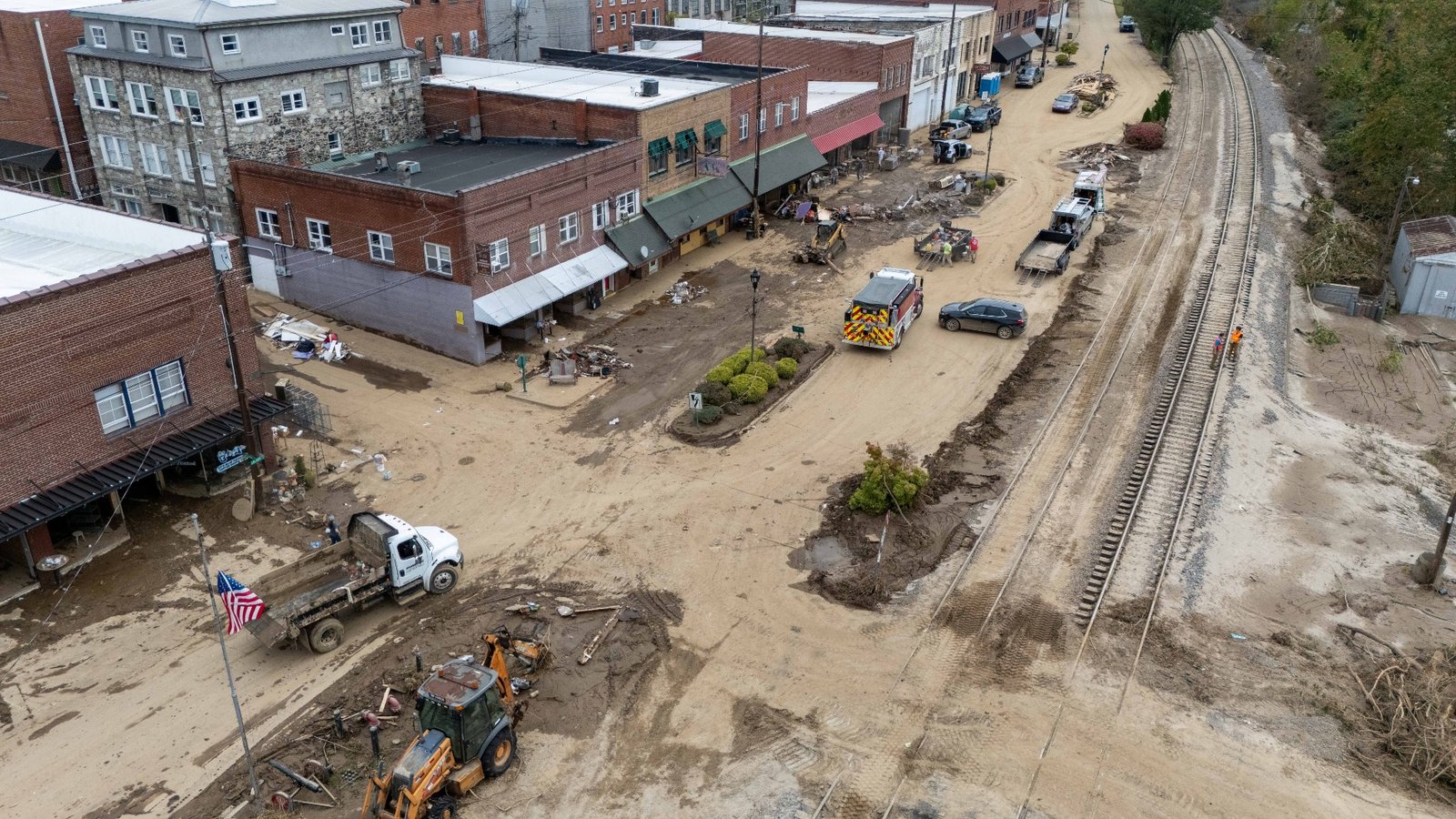 An overhead photo shows a commercial street and railroad track covered in mud and debris.