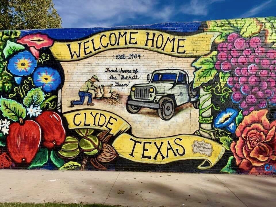 A colorful mural on the side of a building in Clyde, Texas reads "Welcome Home Clyde, Texas"