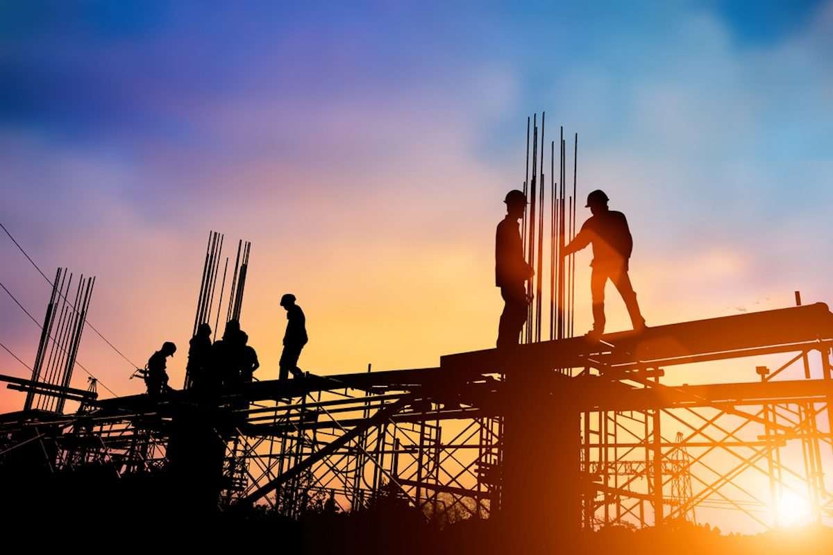 Silhouette of construction site objects and people, with orange-hued sky as a backdrop